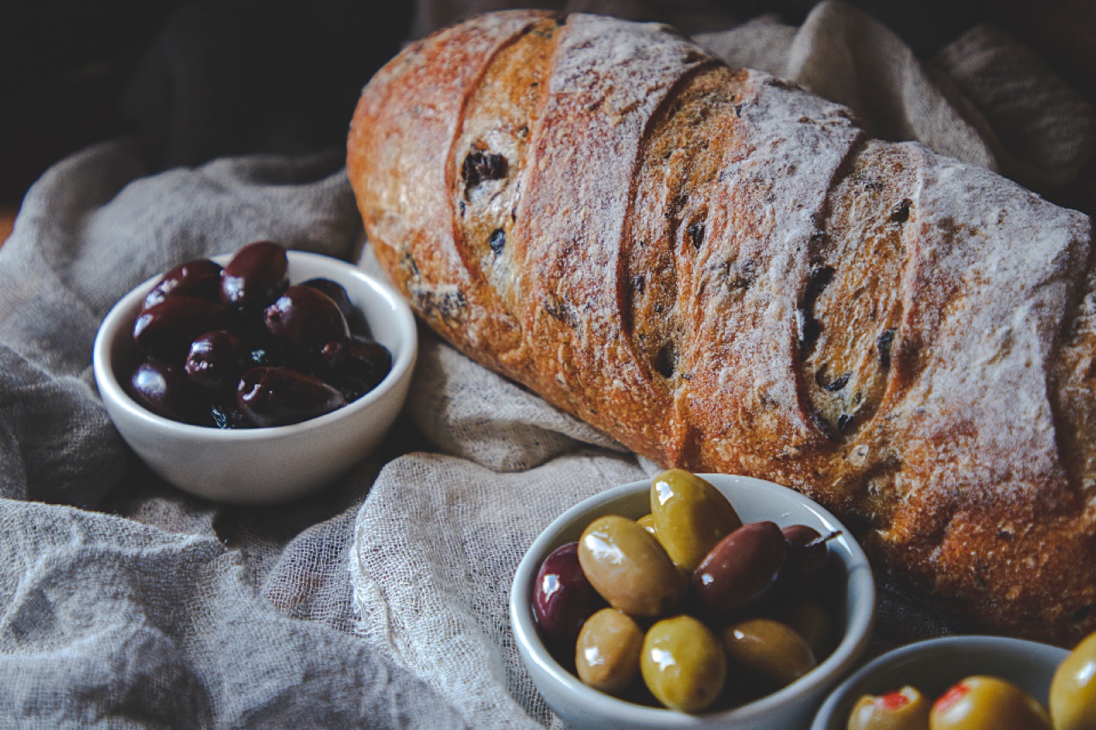 A floured loaf beside small bowls of olives on linen