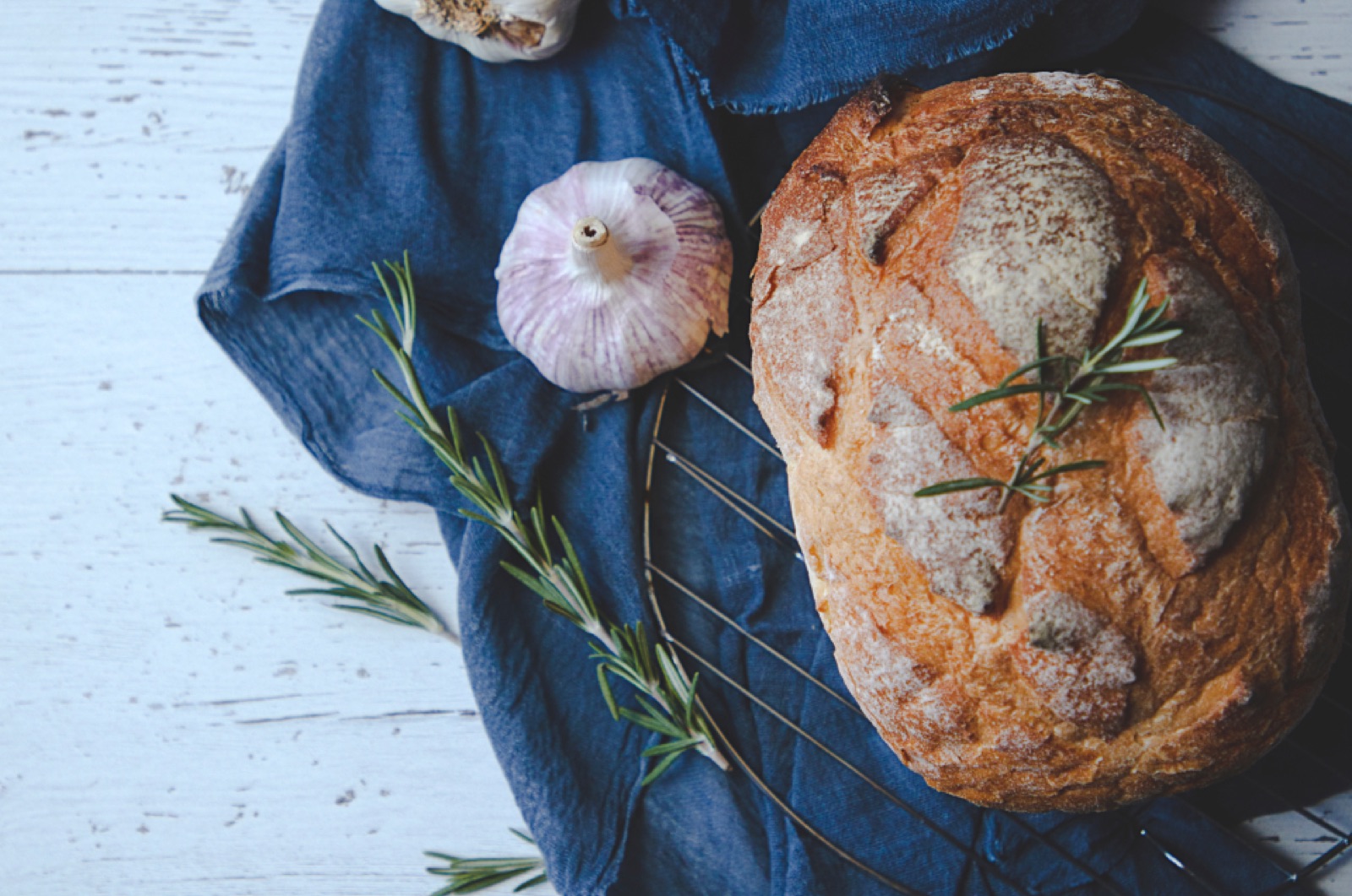A sourdough loaf with garlic and rosemary on a blue cloth