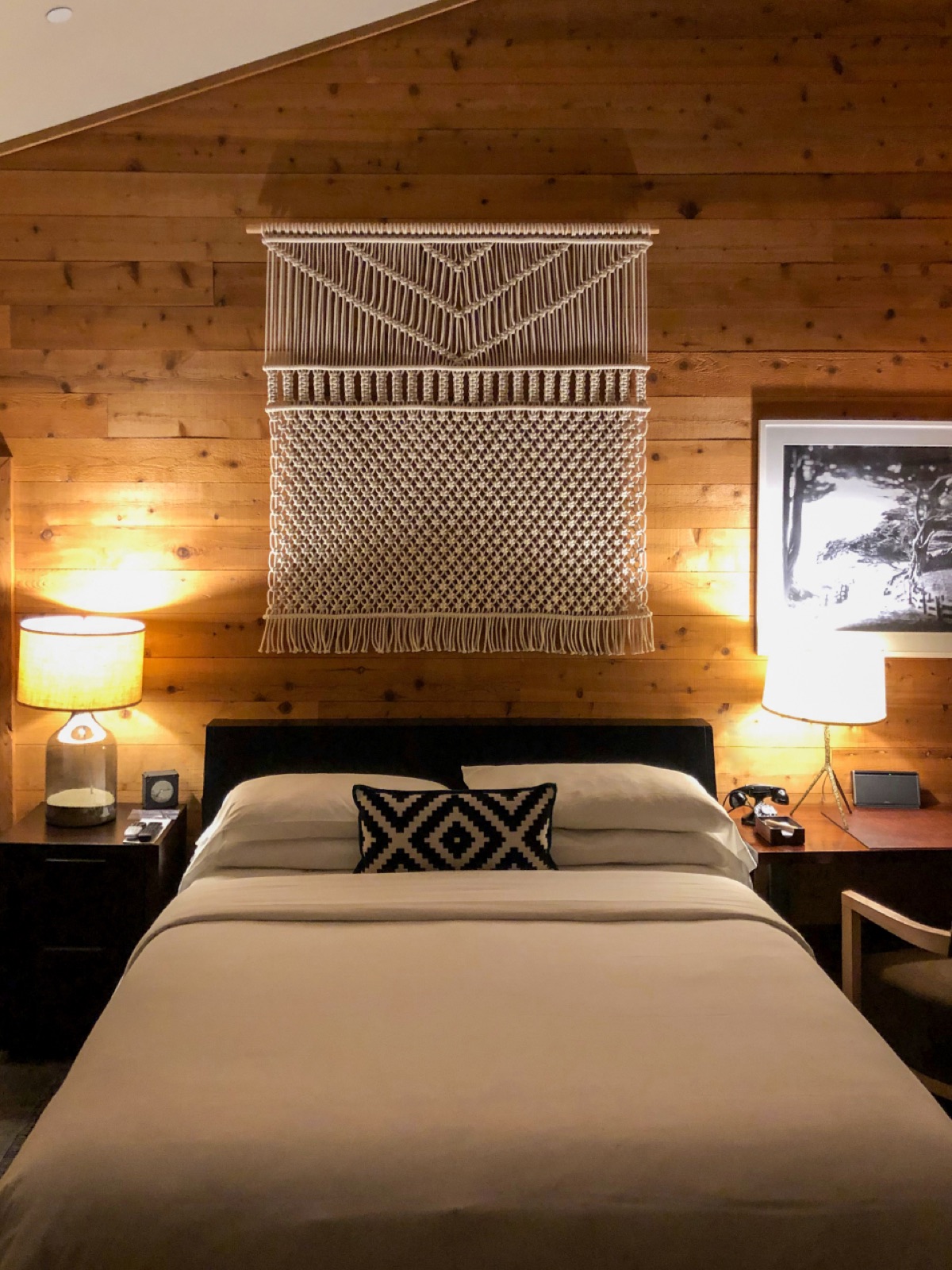 A timber-lined bedroom with a made bed and lit lamps either side